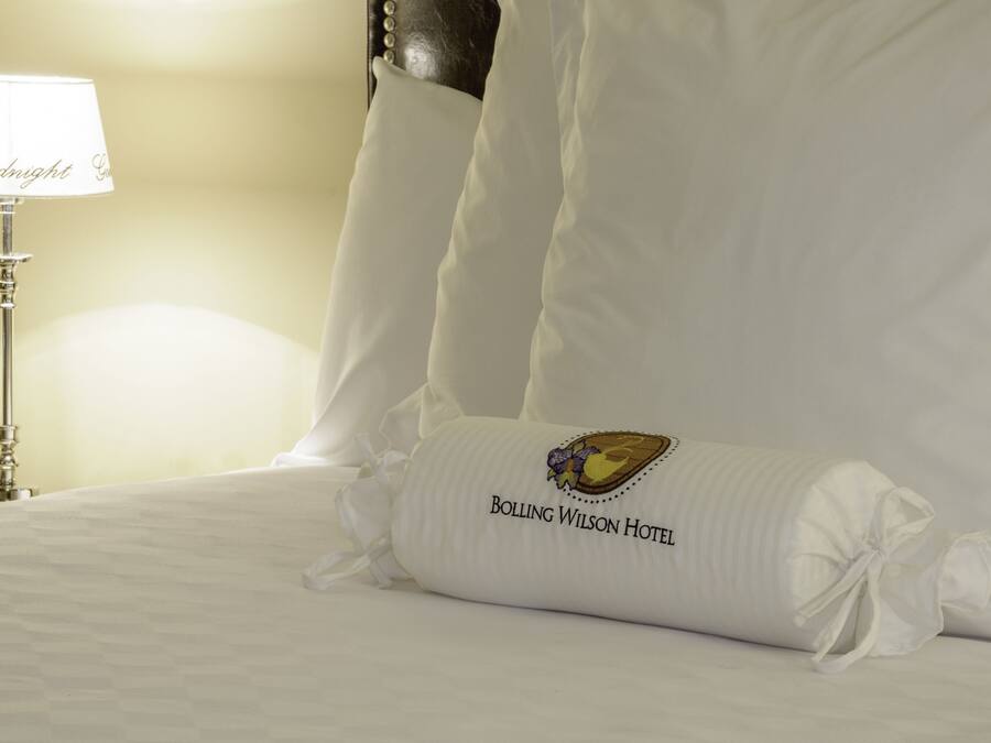 Una cama cuidadosamente hecha con una almohada que dice "Bolling Wilson Hotel" y una lámpara con la palabra "Buenas noches" en su pantalla.
