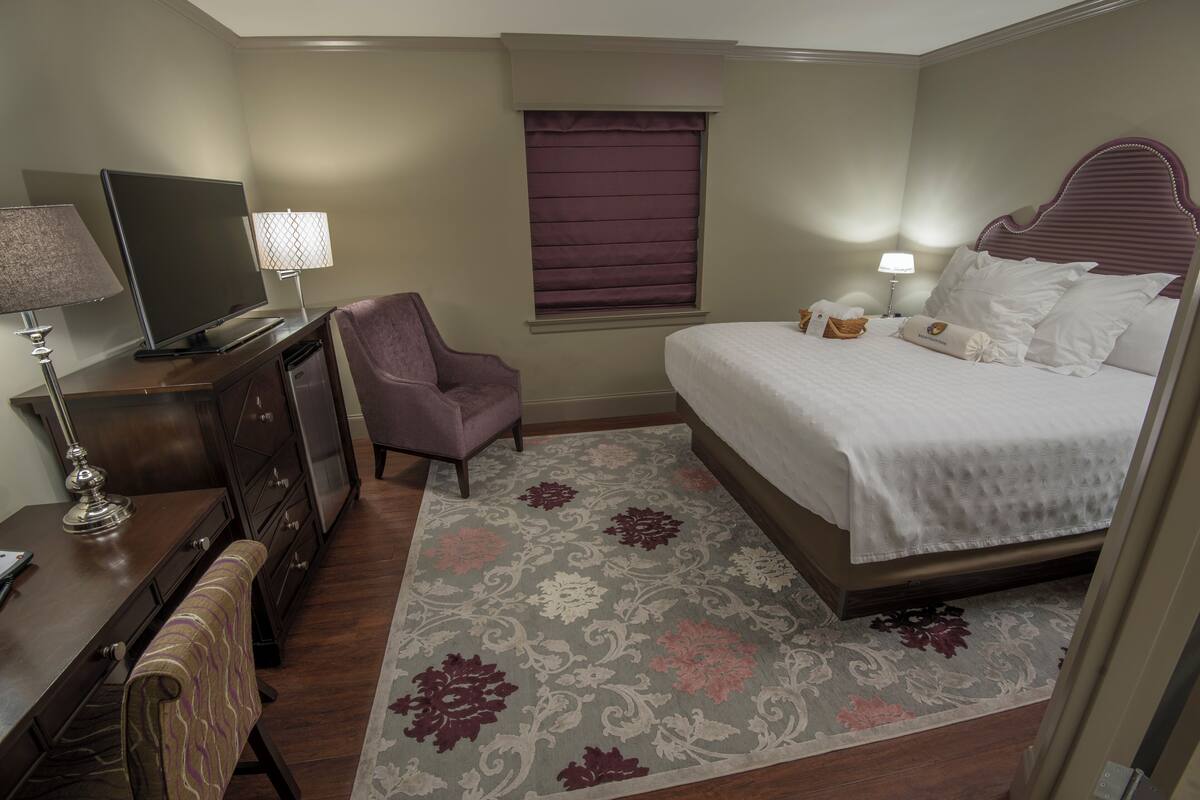 A hotel room with a bed, a desk with a lamp, a chair, a television, and a window with a blind.