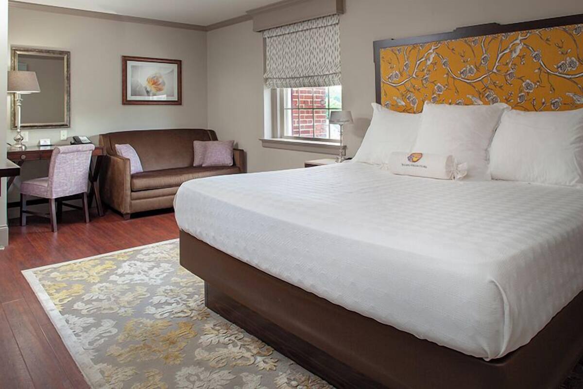 A hotel room with a large bed, a desk, a chair, a sofa, and a window with a view.