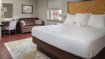 A hotel room with a large bed, a desk, a chair, a sofa, and a window with a view.