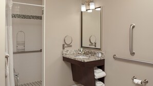 Une salle de bain équipée d’une douche, d’un lavabo avec un miroir et d’une barre d’appui.