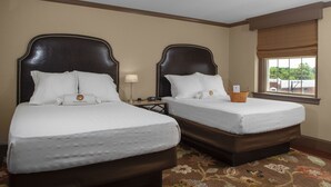 Une chambre d’hôtel avec deux lits, un tapis à motifs floraux, une fenêtre donnant sur un beau paysage et une table de chevet avec une lampe.