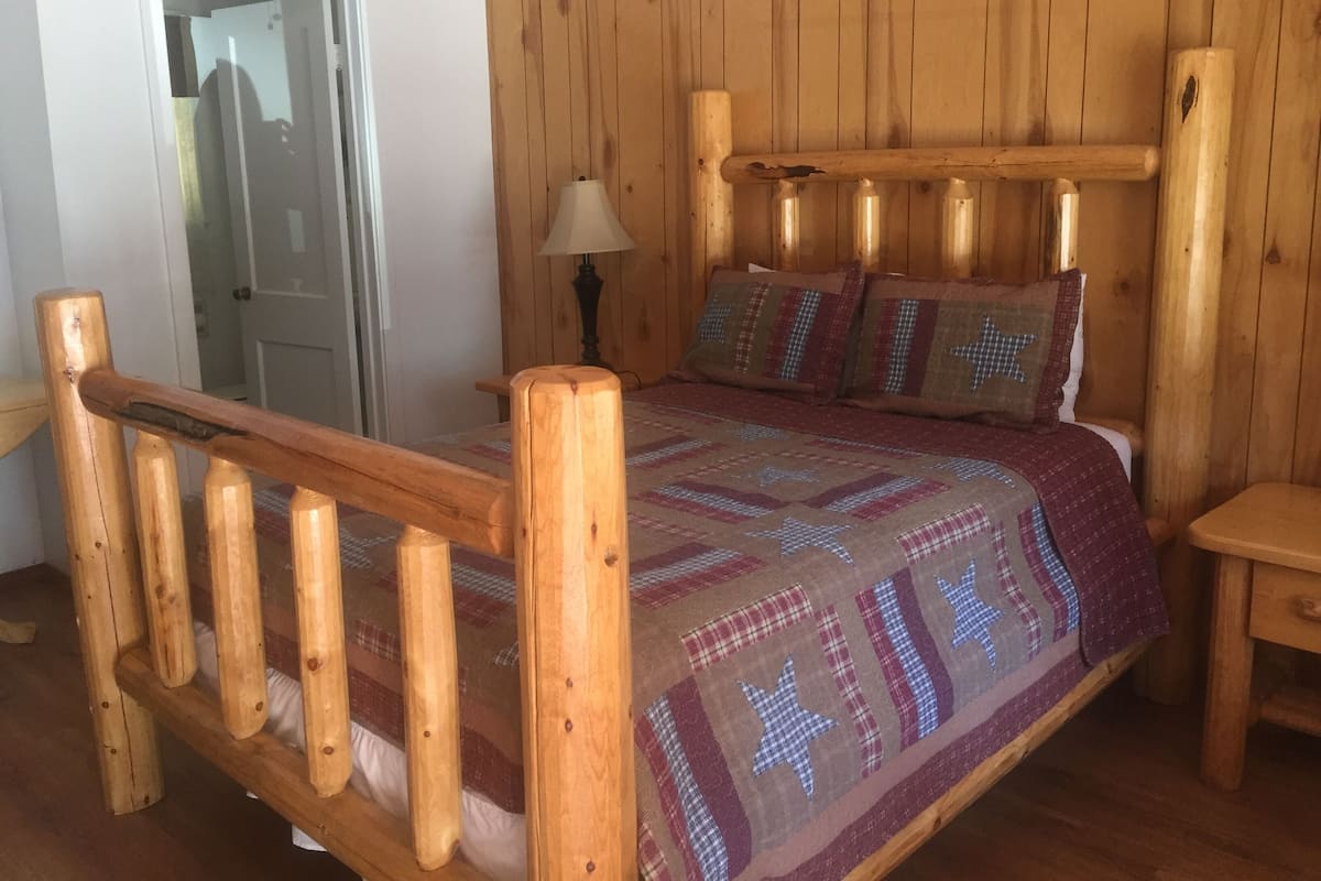 A wooden-framed bed with a quilted bedspread, a nightstand, and a lamp.