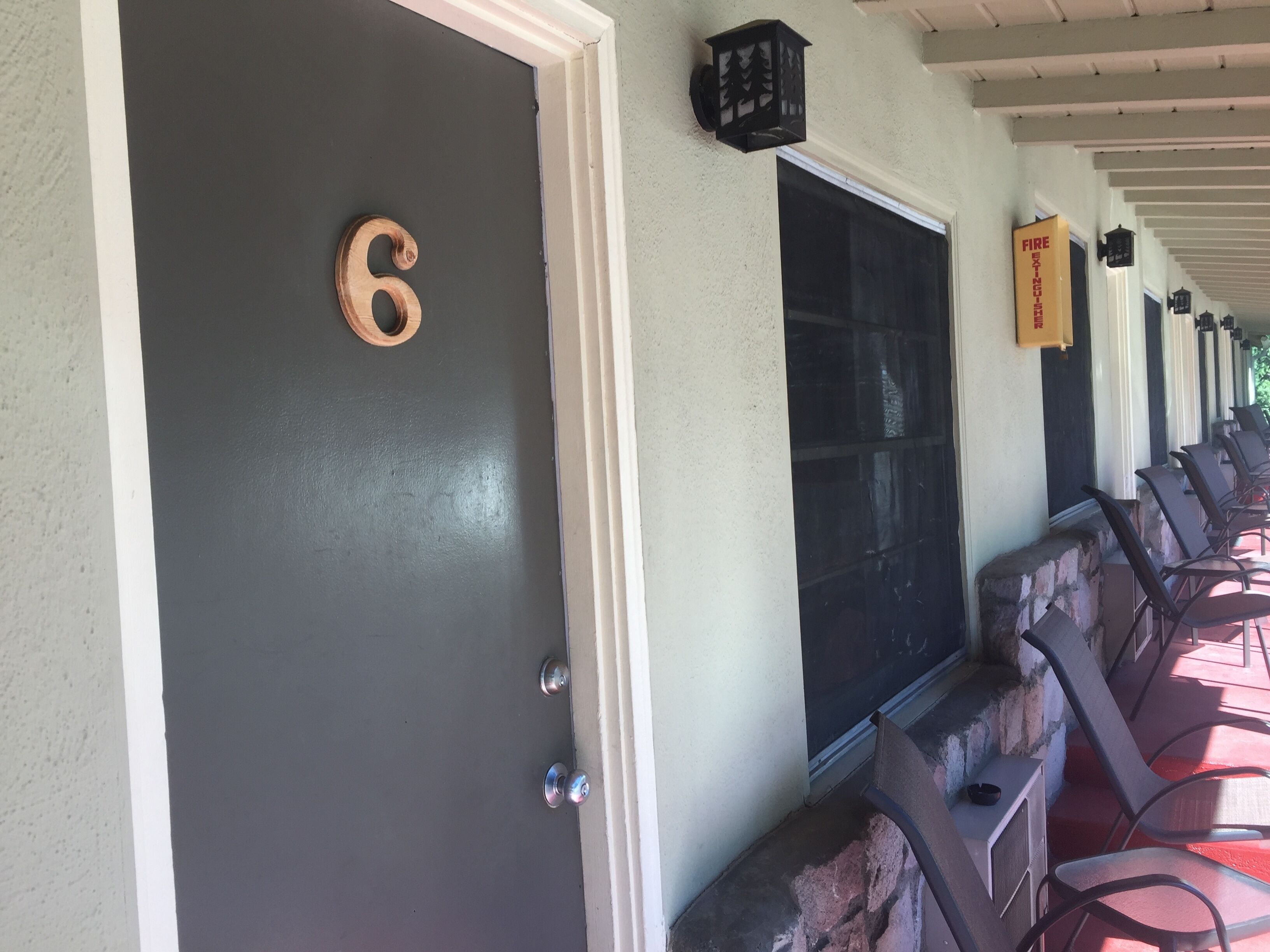 A covered porch with numbered doors, outdoor seating, and a fire extinguisher.