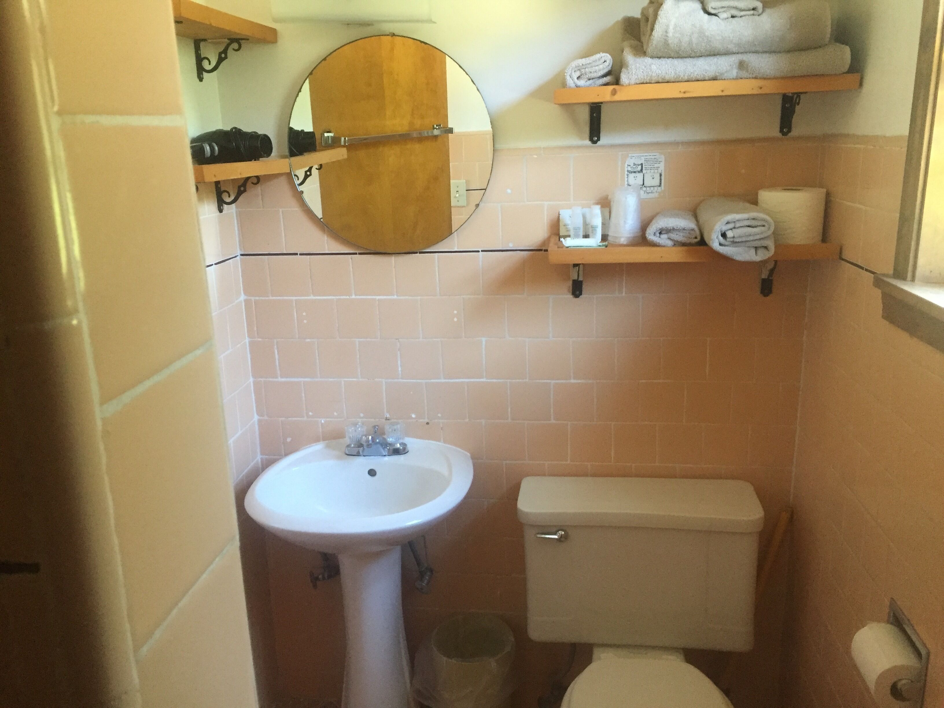 A bathroom with a white sink, a toilet, and a mirror above the sink. There are shelves above the mirror holding towels and toiletries.
