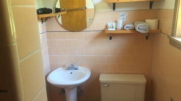 A bathroom with a white sink, a toilet, and a mirror above the sink. There are shelves above the mirror holding towels and toiletries.