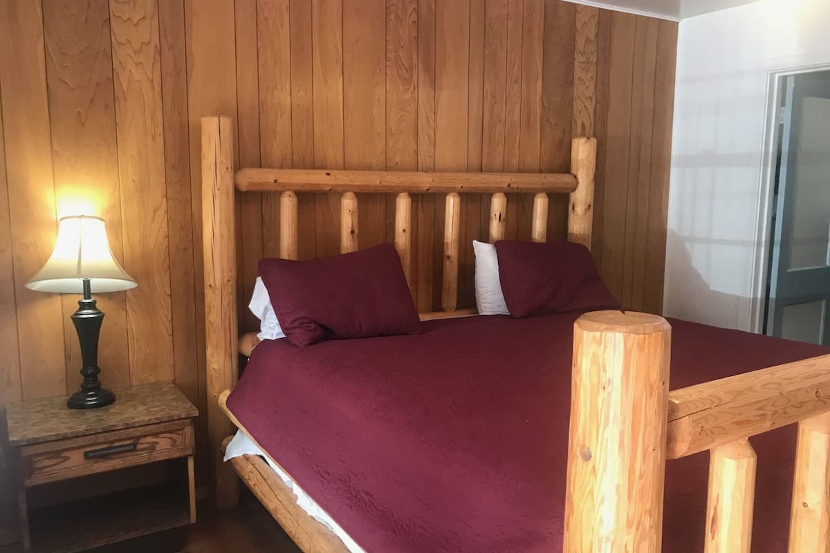 A wooden bed with a headboard, a bedside table with a lamp, and a window with a curtain.