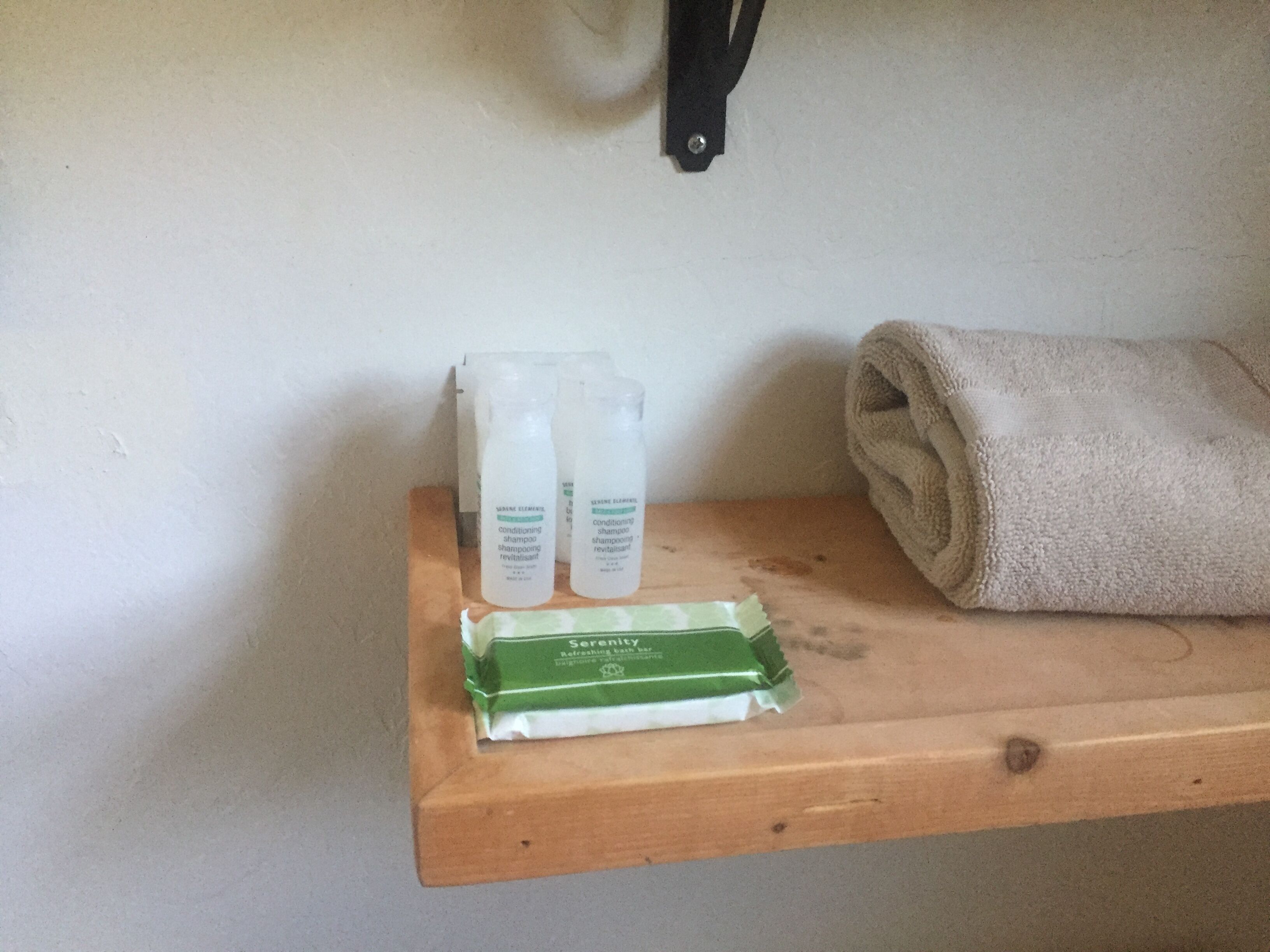 A wooden shelf with three bottles of shampoo and a green bar of soap.