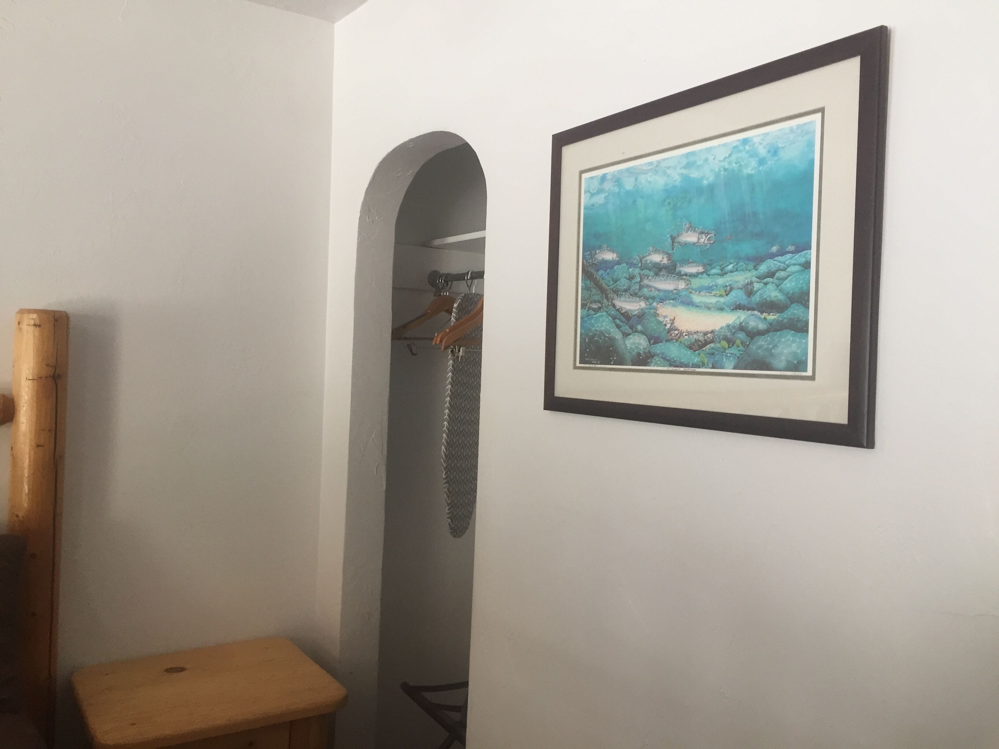 A bathroom with a wooden bench, a towel rack, and a framed painting of an underwater scene.