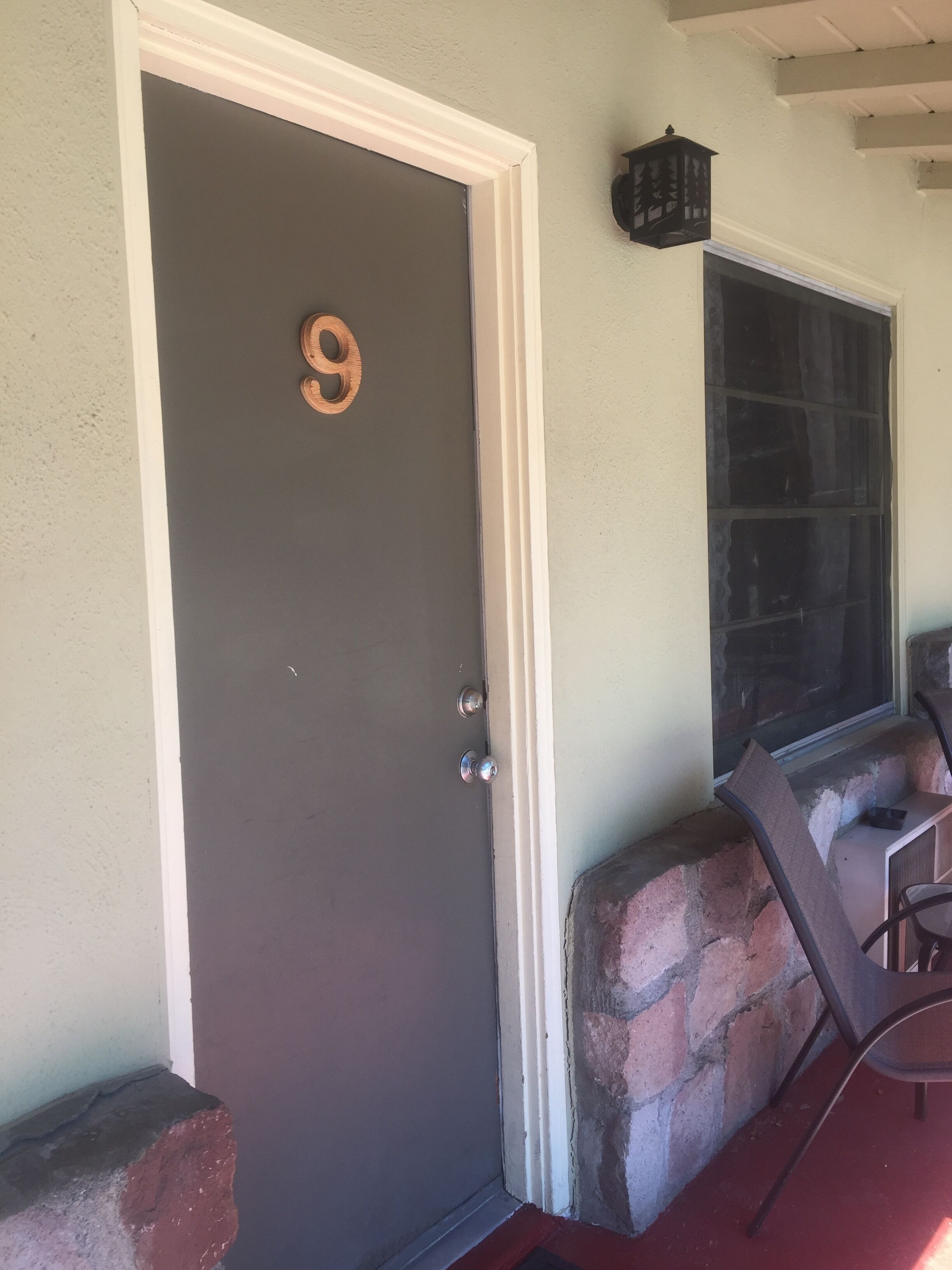 A dark grey door with a wooden number '9' sign, a white door frame, and a stone bench with a metal chair.