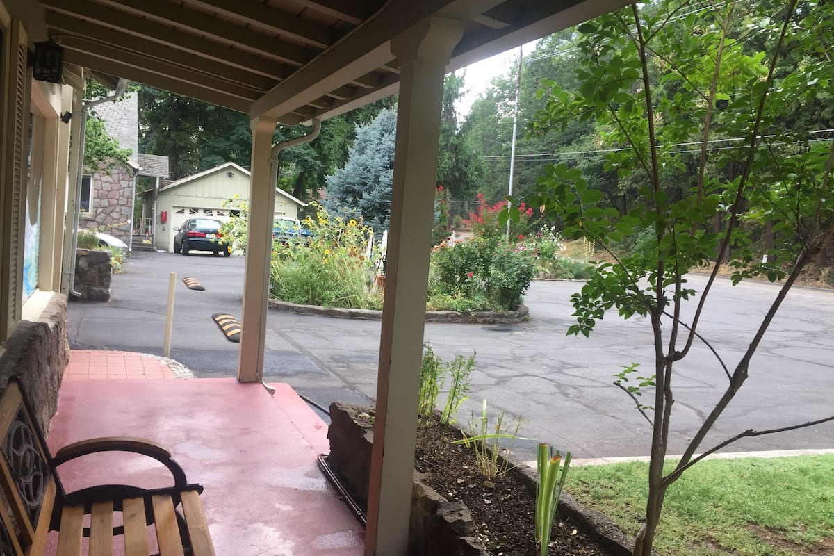 A covered porch with a bench, a parking lot, and a view of a residential street with houses and greenery.