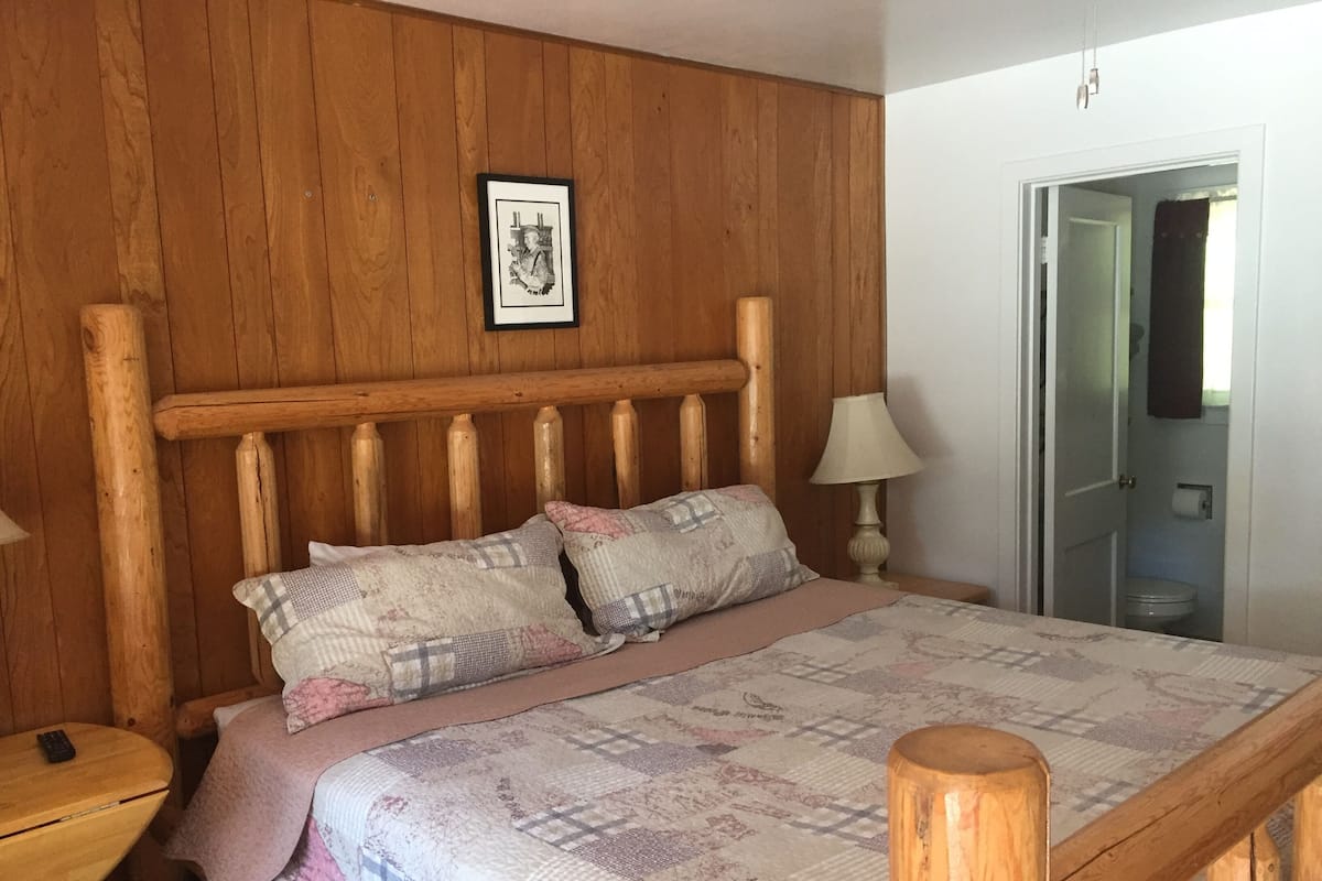 A wooden bed with a headboard, two pillows, a bedside lamp, and a quilt.