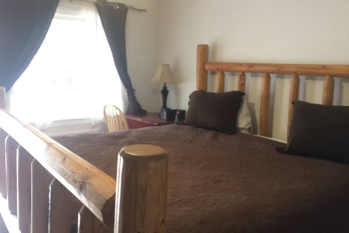 A bedroom with a wooden headboard, a bed with a brown cover, a nightstand with a lamp, and a chair.