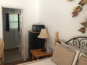 A bedroom with a bed, a wooden nightstand, a lamp, a dresser, and a microwave on top of it. - Dunsmuir Lodge (Dunsmuir)