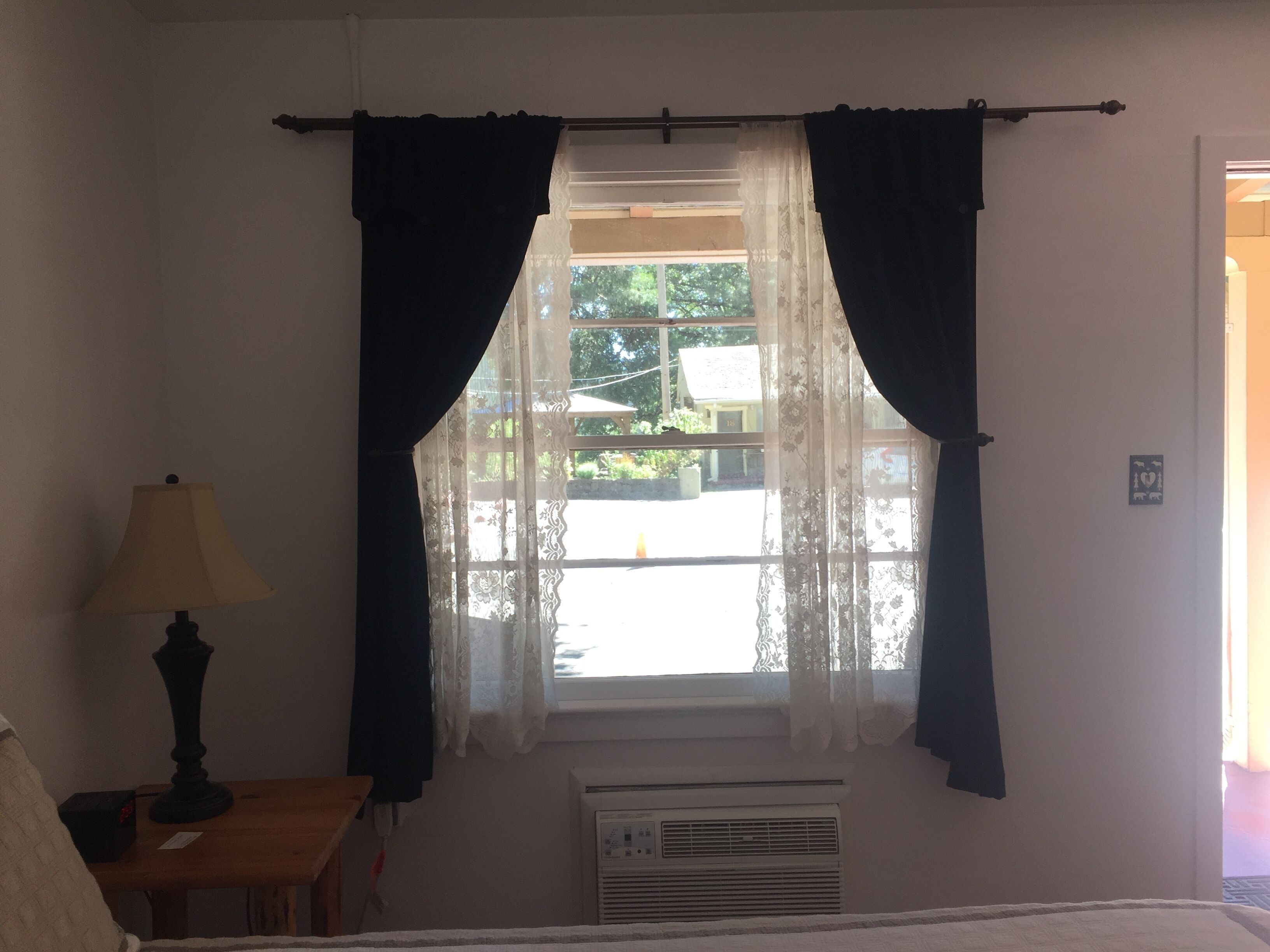 Een kamer met een raam, een lamp en een airconditioning.