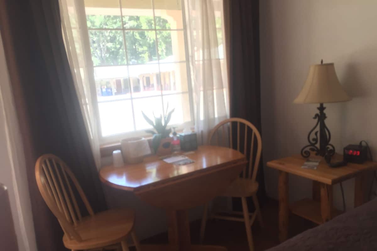 A room with a wooden table, two chairs, a lamp, and a window with curtains.