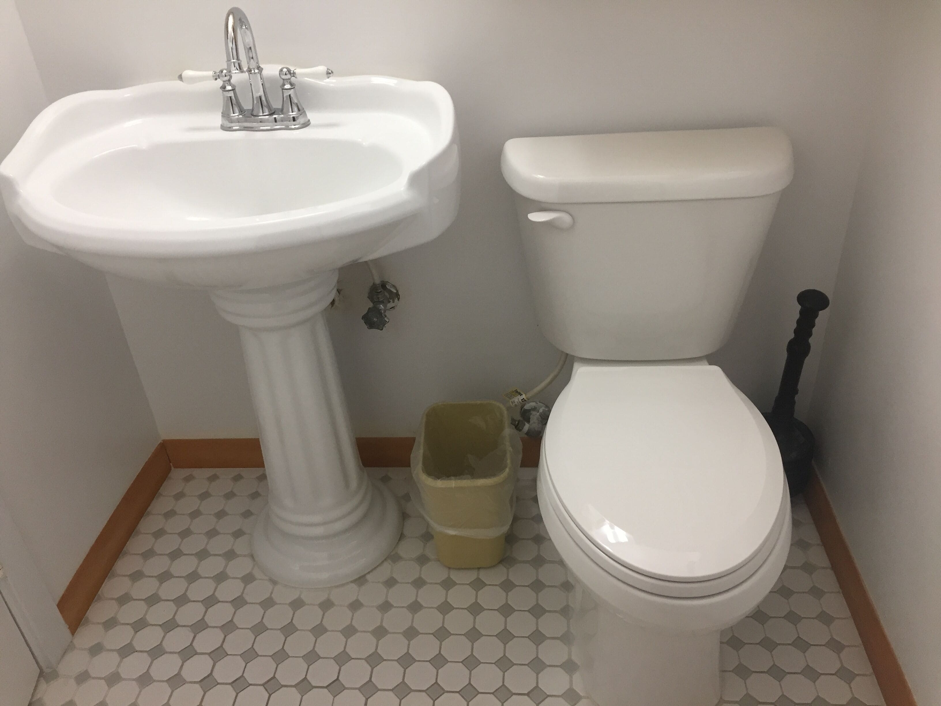 Een badkamer met een wastafel op een voetstuk, toilet en een afvalbak.