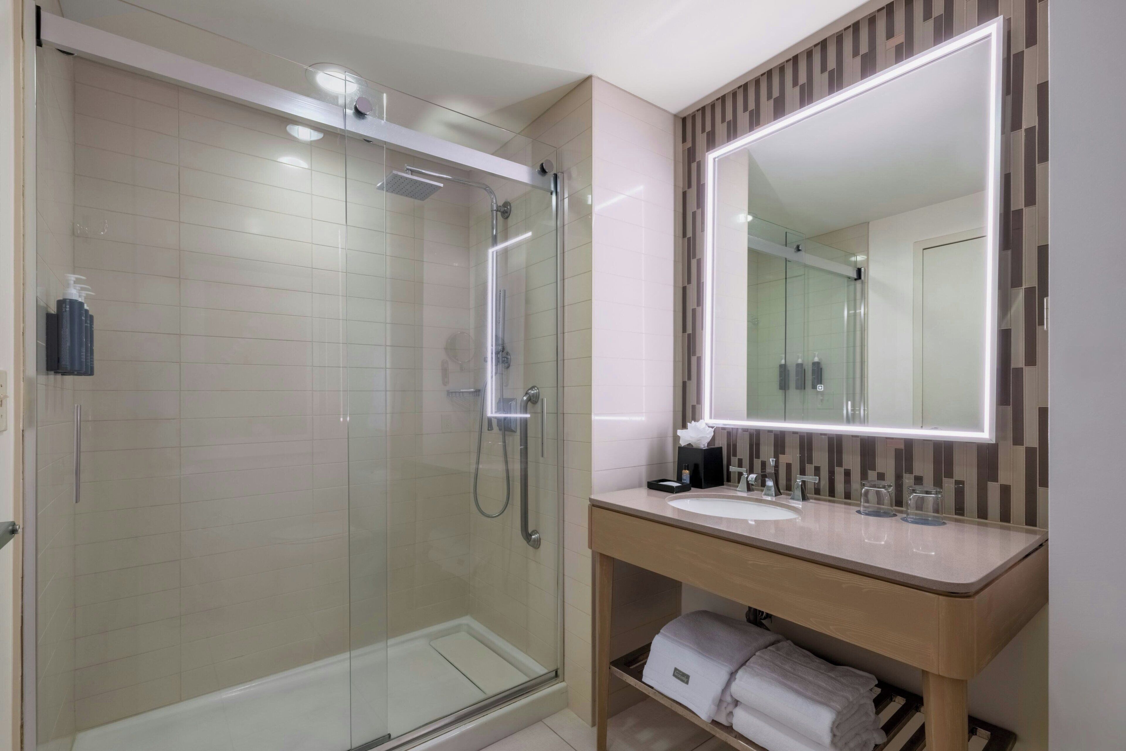 A modern bathroom with a glass-enclosed shower, a vanity with a mirror, and neatly folded towels on a shelf.