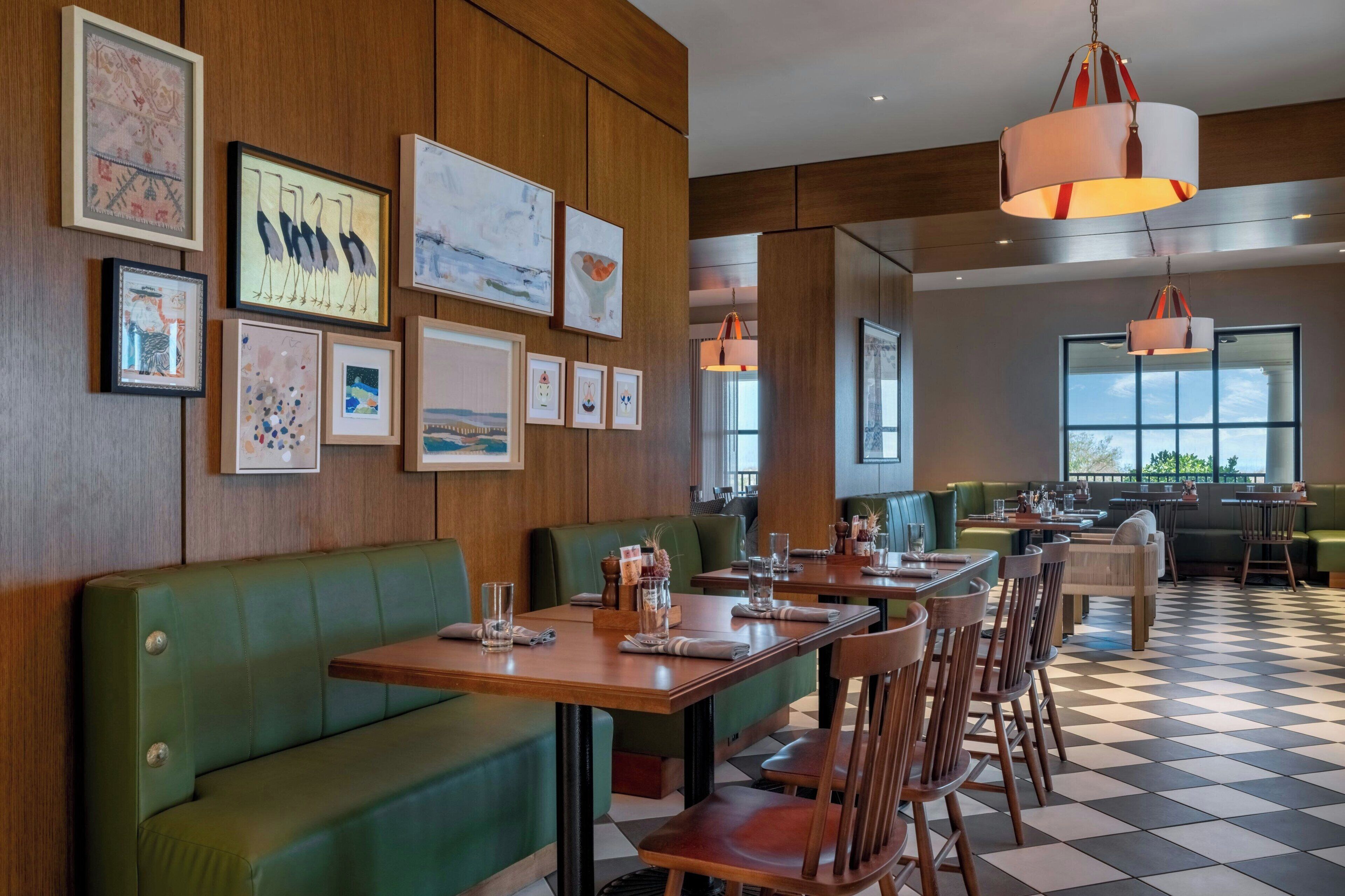 Ein Restaurant mit Holzwandverkleidung, grün gepolsterten Sitzgelegenheiten und Kunstwerken. Die Tische sind mit Gläsern und Besteck gedeckt.
