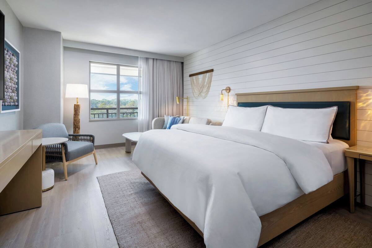 Une chambre d’hôtel avec un grand lit, un bureau, une chaise et une fenêtre avec des rideaux.