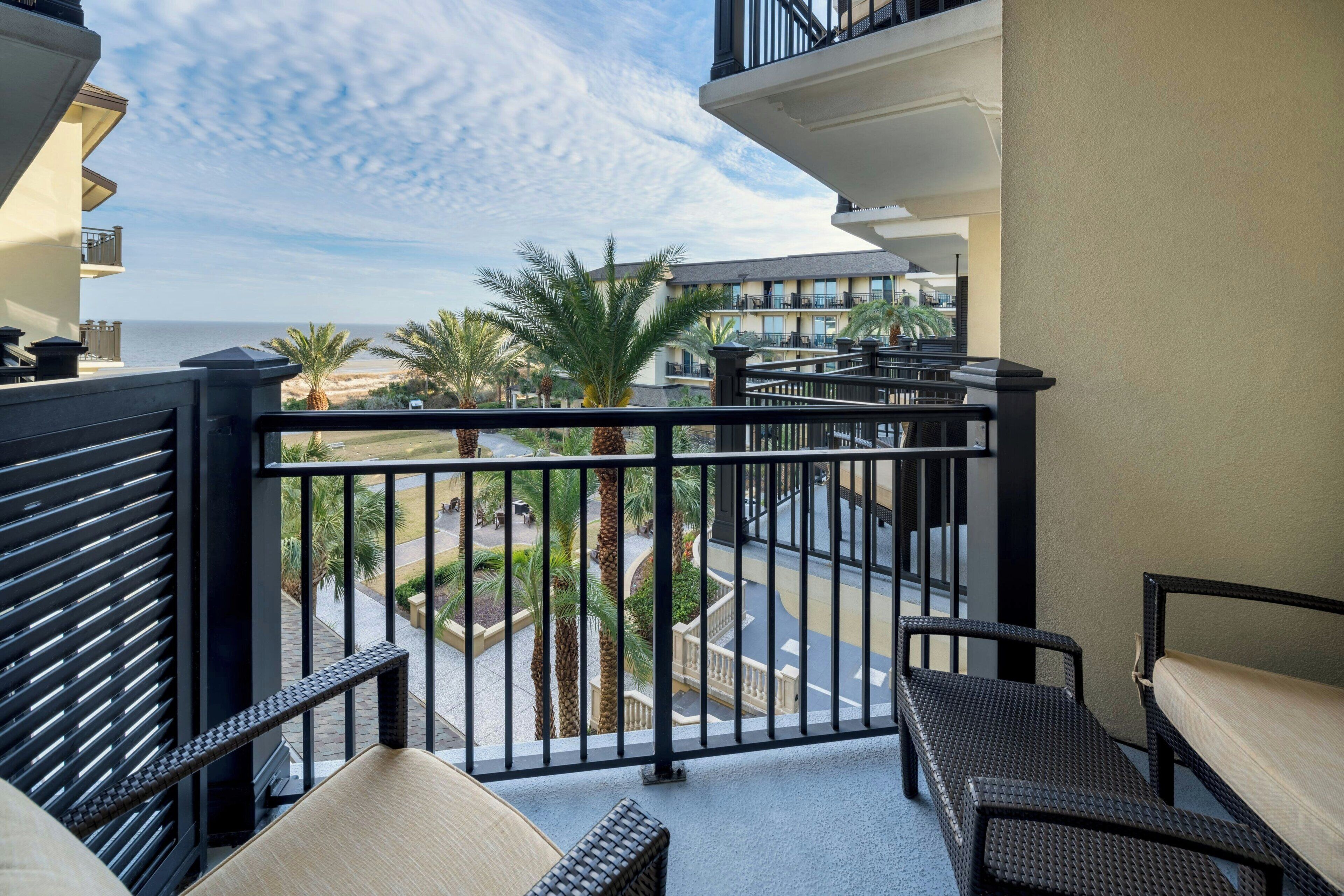 A balcony with a view of the ocean, palm trees, and a street.