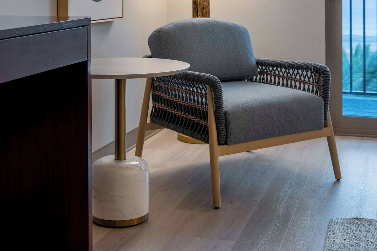 Un salon moderne avec un canapé gris, une table ronde et une lampe. Des tableaux abstraits ornent le mur, et une porte-fenêtre donne sur l’extérieur.