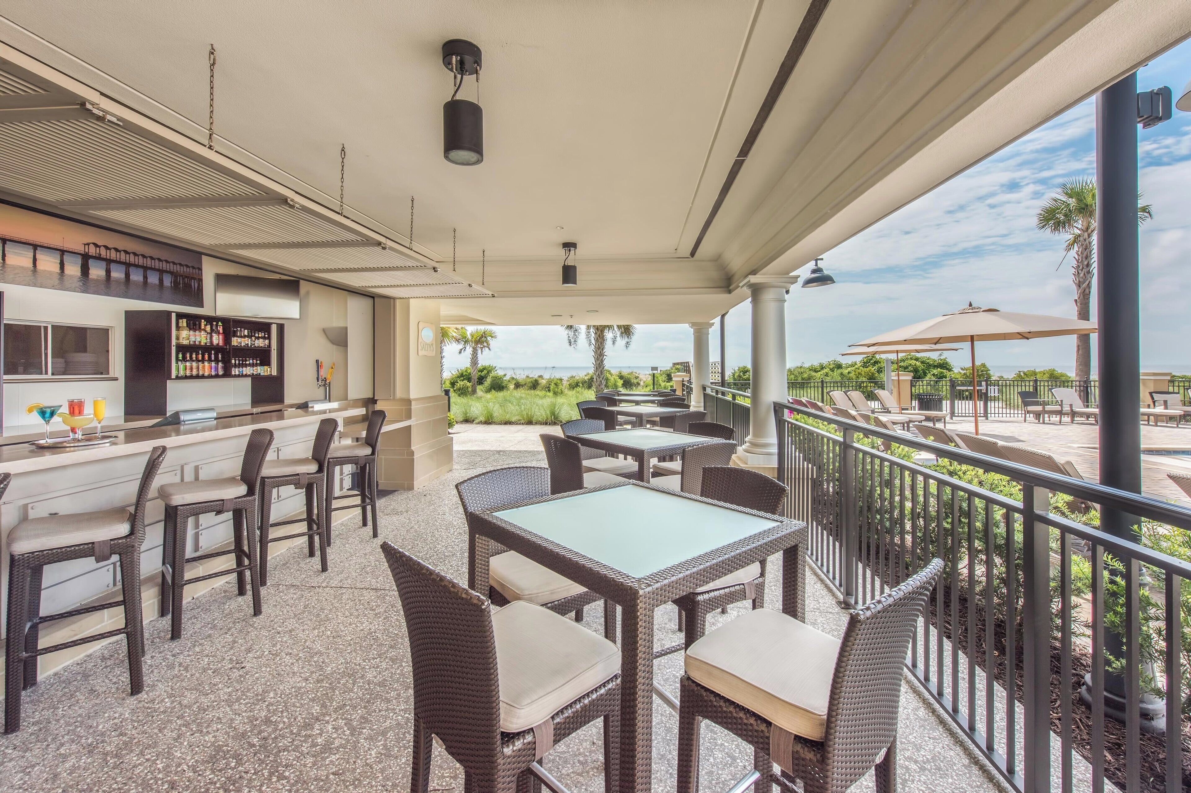 A covered outdoor seating area with wicker furniture and a bar.