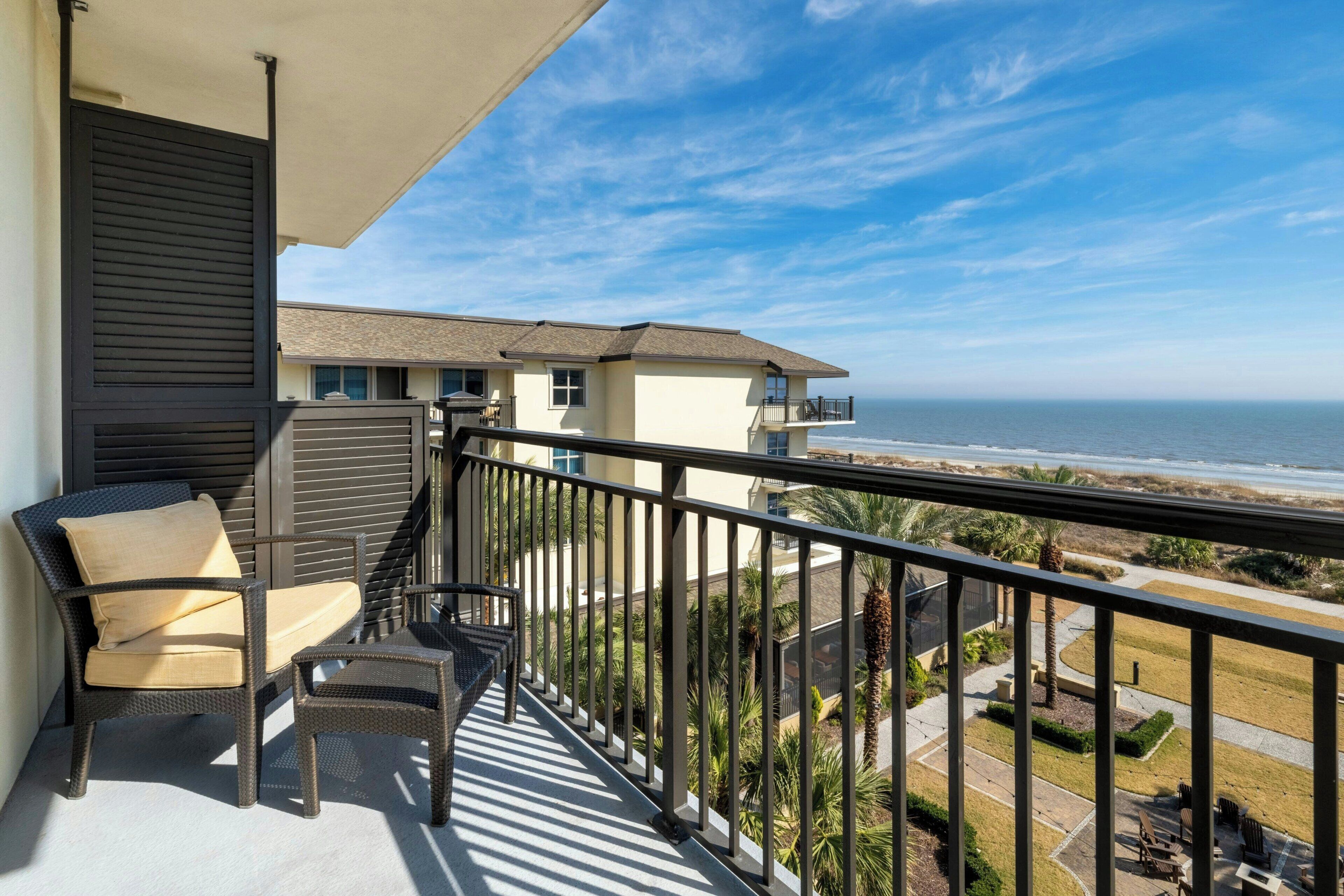 A balcony with wicker furniture, a view of the ocean, and a building with a balcony.