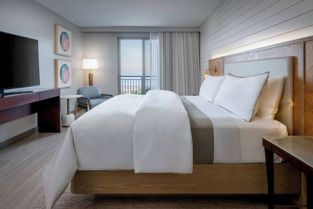 Une chambre d’hôtel moderne dotée d’un grand lit, d’une télévision à écran plat, d’un bureau et offrant une vue sur l’extérieur.