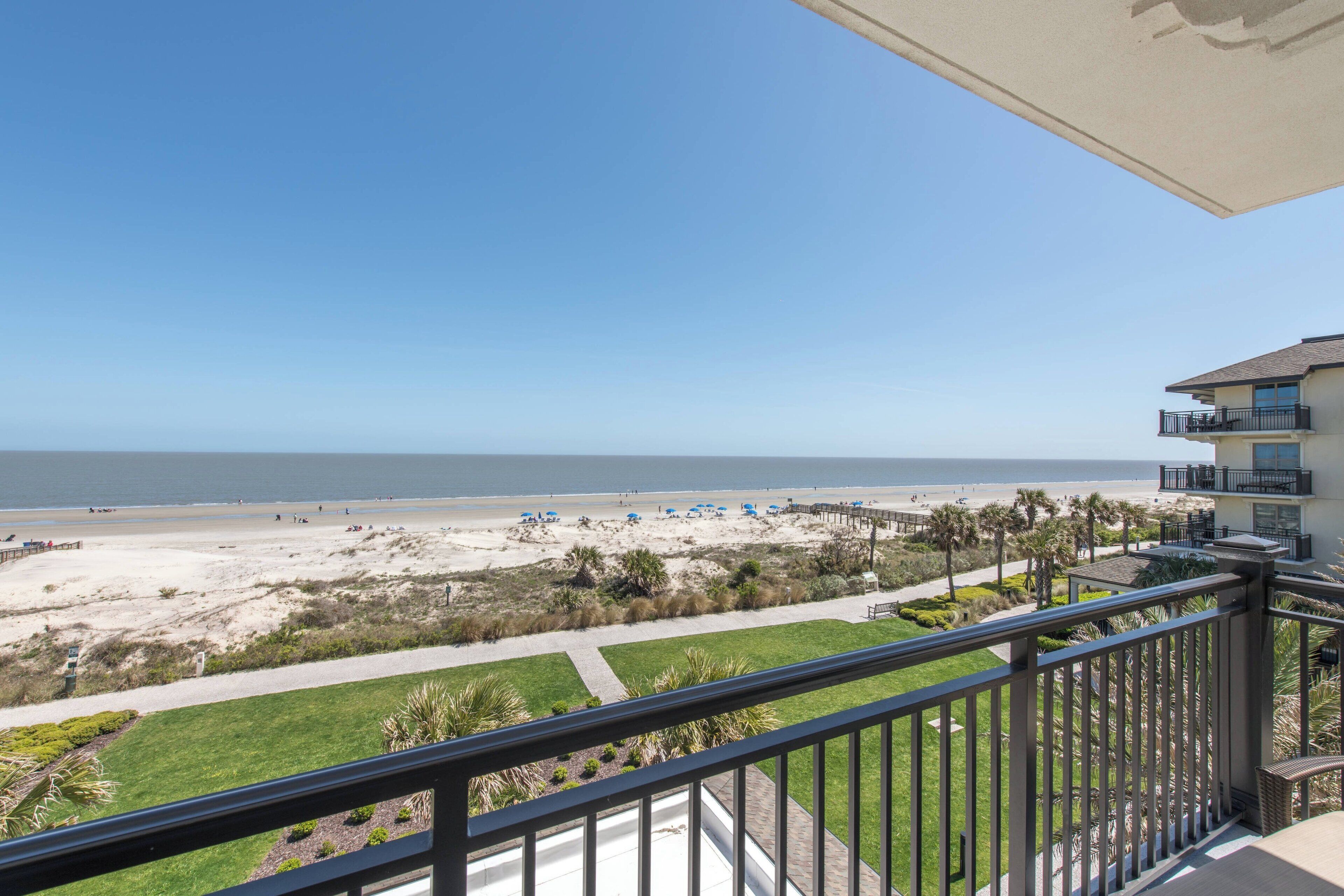 A balcony with a view of a beach, a clear sky, and a building with a balcony.