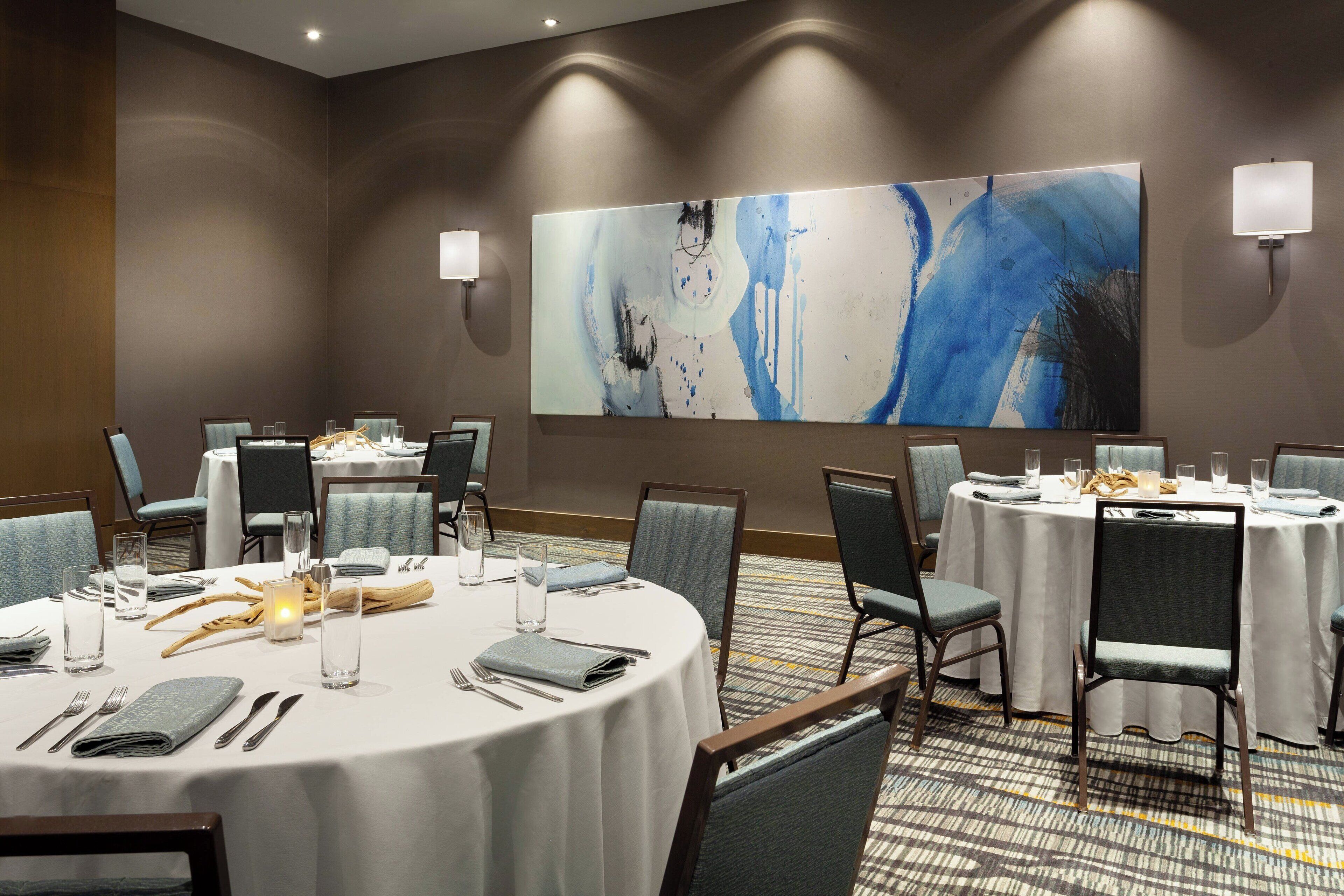 Une salle de conférence avec des tables rondes, des chaises et un grand tableau abstrait accroché au mur.