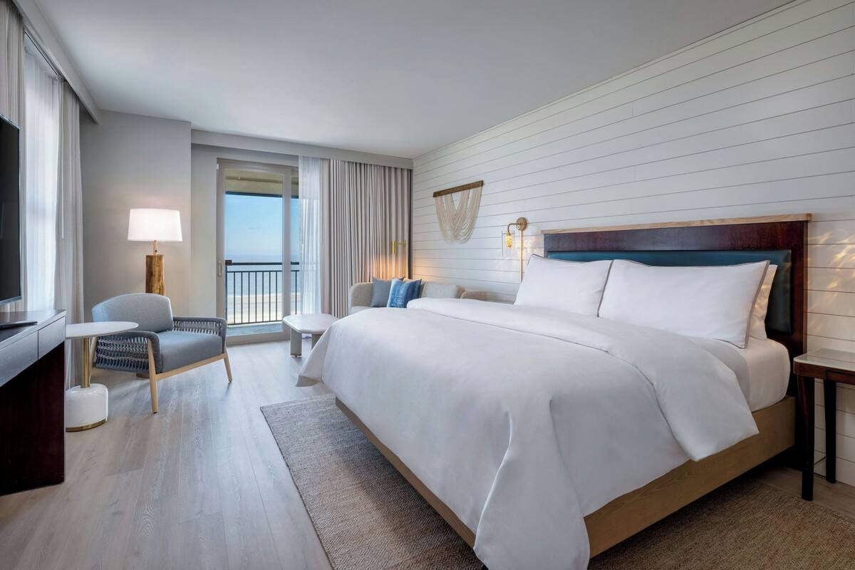 Une chambre d’hôtel avec un grand lit, un bureau, une chaise, une lampe et une vue sur l’extérieur.