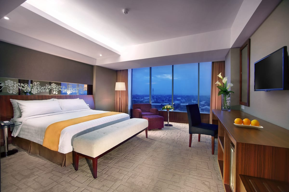 A hotel room with a large bed, a desk, a chair, and a TV.
