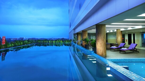 A rooftop infinity pool with a glass barrier, lounge chairs, and a view of the cityscape. - Aston Madiun Hotel & Conference Center (Madiun)