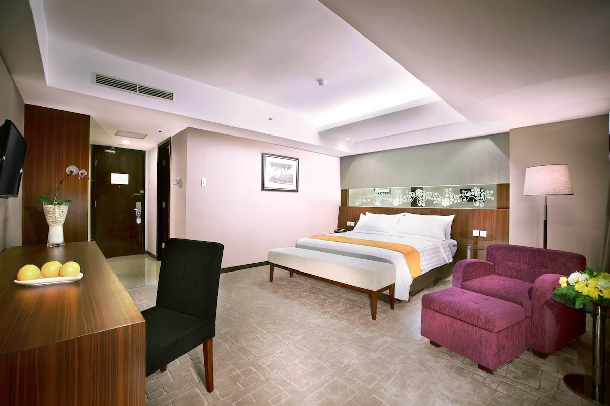A hotel room with a bed, a desk with a chair, a sofa, and a small table with flowers.