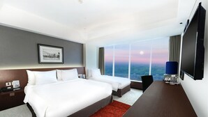 A hotel room with a large bed, a desk, and a TV. There is a window with a view of the city and a moon in the sky. - Aston Madiun Hotel & Conference Center (Madiun)