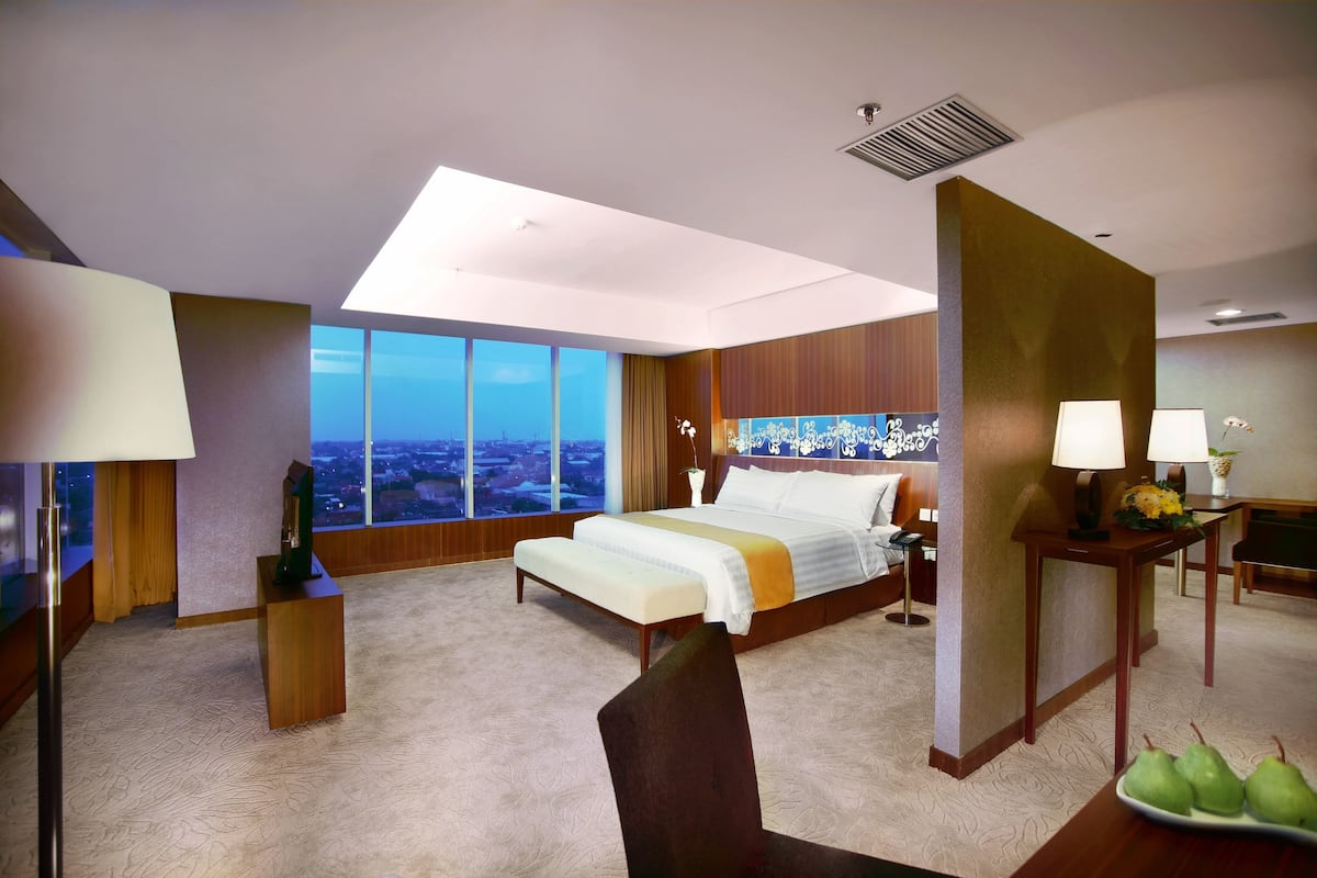 A modern hotel room with a large bed, a desk, a chair, and a view of the city.