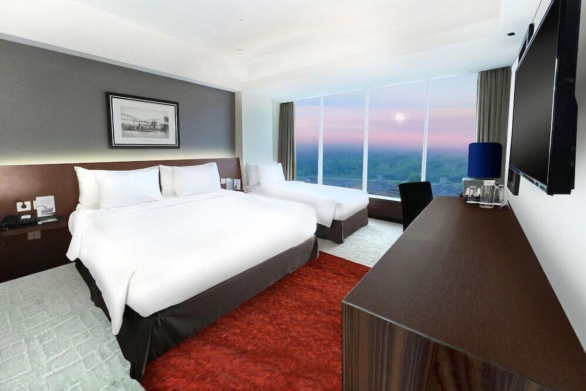 A hotel room with a large bed, a desk, a TV, and a city view.