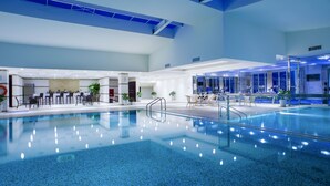 Una piscina interior con agua cristalina, rodeada de zonas de estar y un mostrador de recepción.