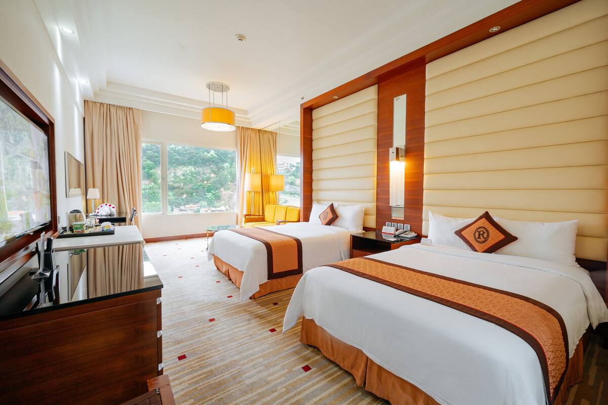A hotel room with two beds, a desk, a chair, and a large window.