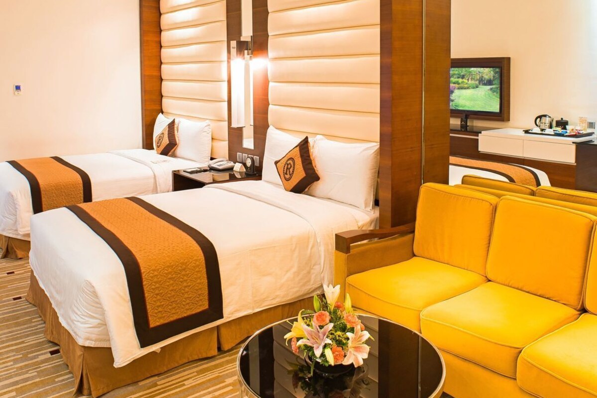 A hotel room with two beds, a sofa, a TV, and a coffee table.
