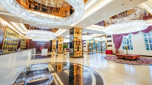 Un vestíbulo amplio con un piso circular reflectante en el centro, varios candelabros y una zona de estar con un sofá tapizado en rojo.