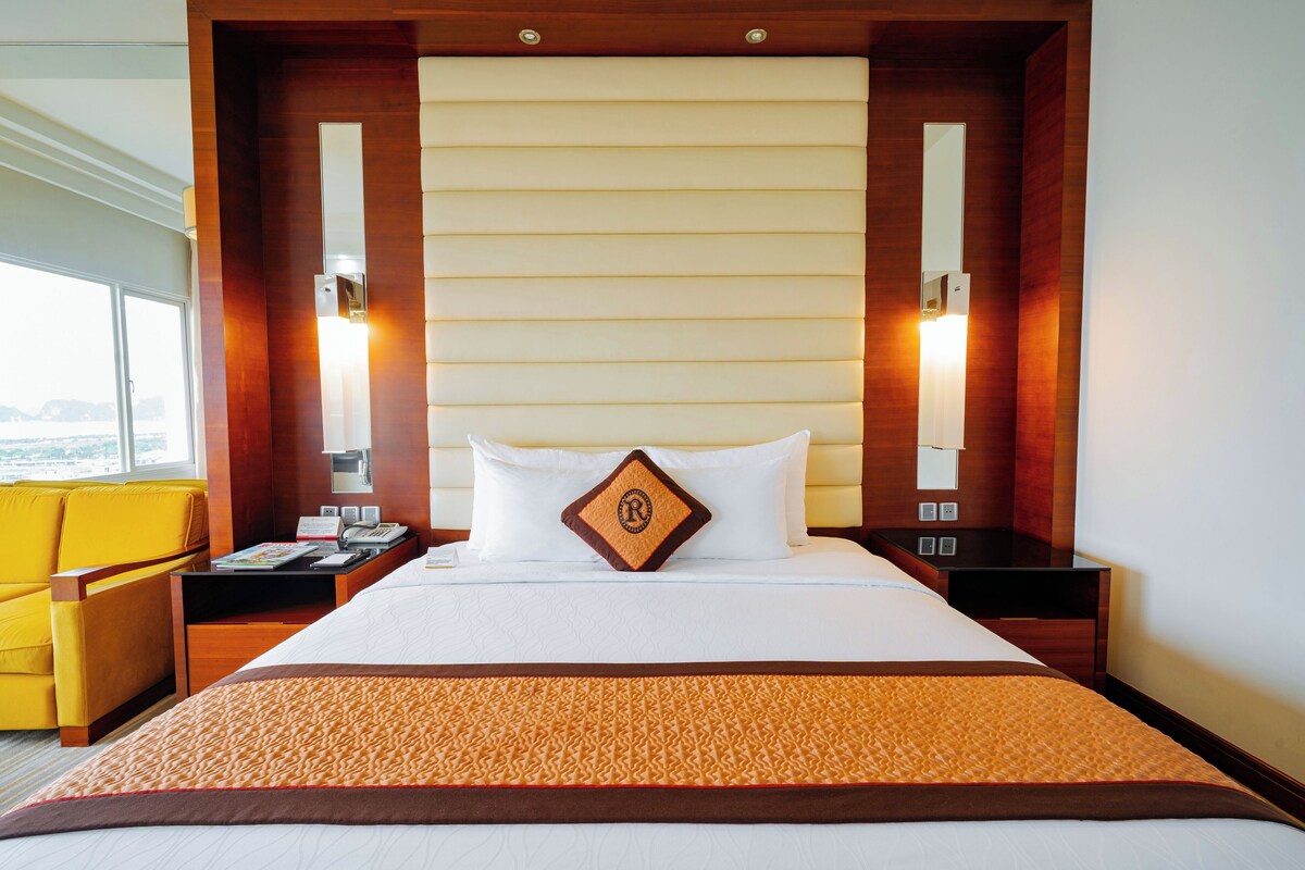 A hotel room with a large bed, a bedside table, a chair, and a window with a view.