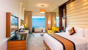 Habitación de hotel con cama, escritorio, silla, lámpara y vista al mar.