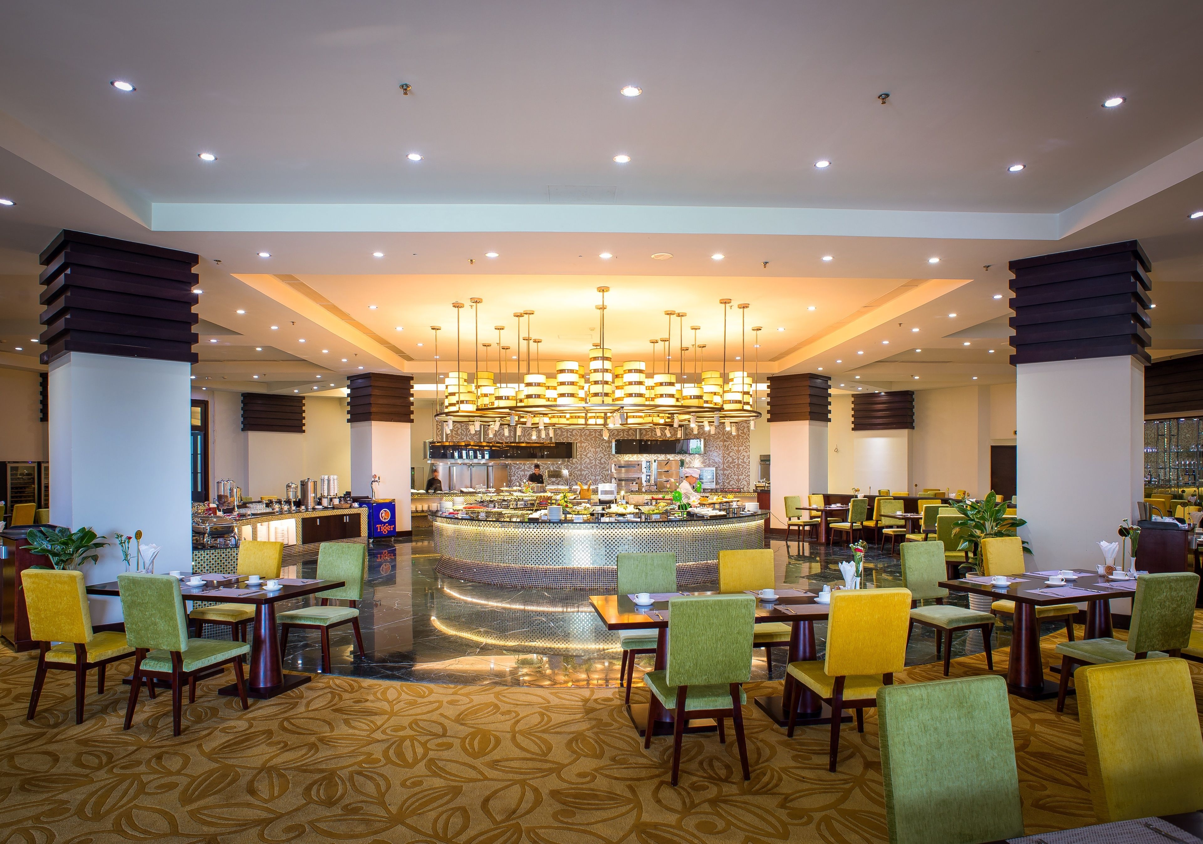 Un amplio vestíbulo de hotel con una zona de bar central, varios conjuntos de asientos y una alfombra estampada.