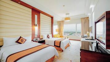 A hotel room with two beds, a desk, a chair, a TV, and a large window offering a city view.