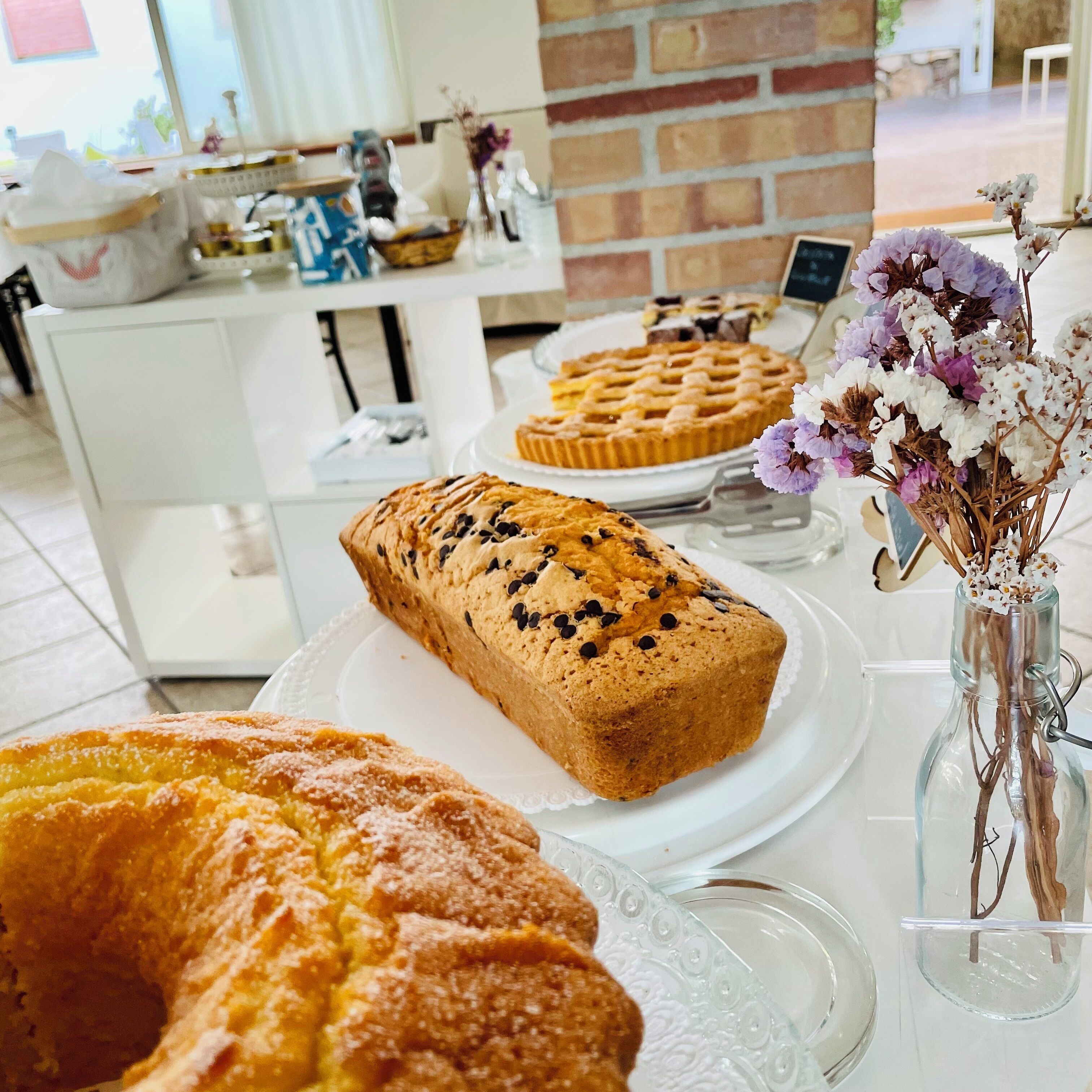 Una mesa con varios productos horneados, incluyendo una hogaza de pan y una tarta, además de un florero con flores secas.