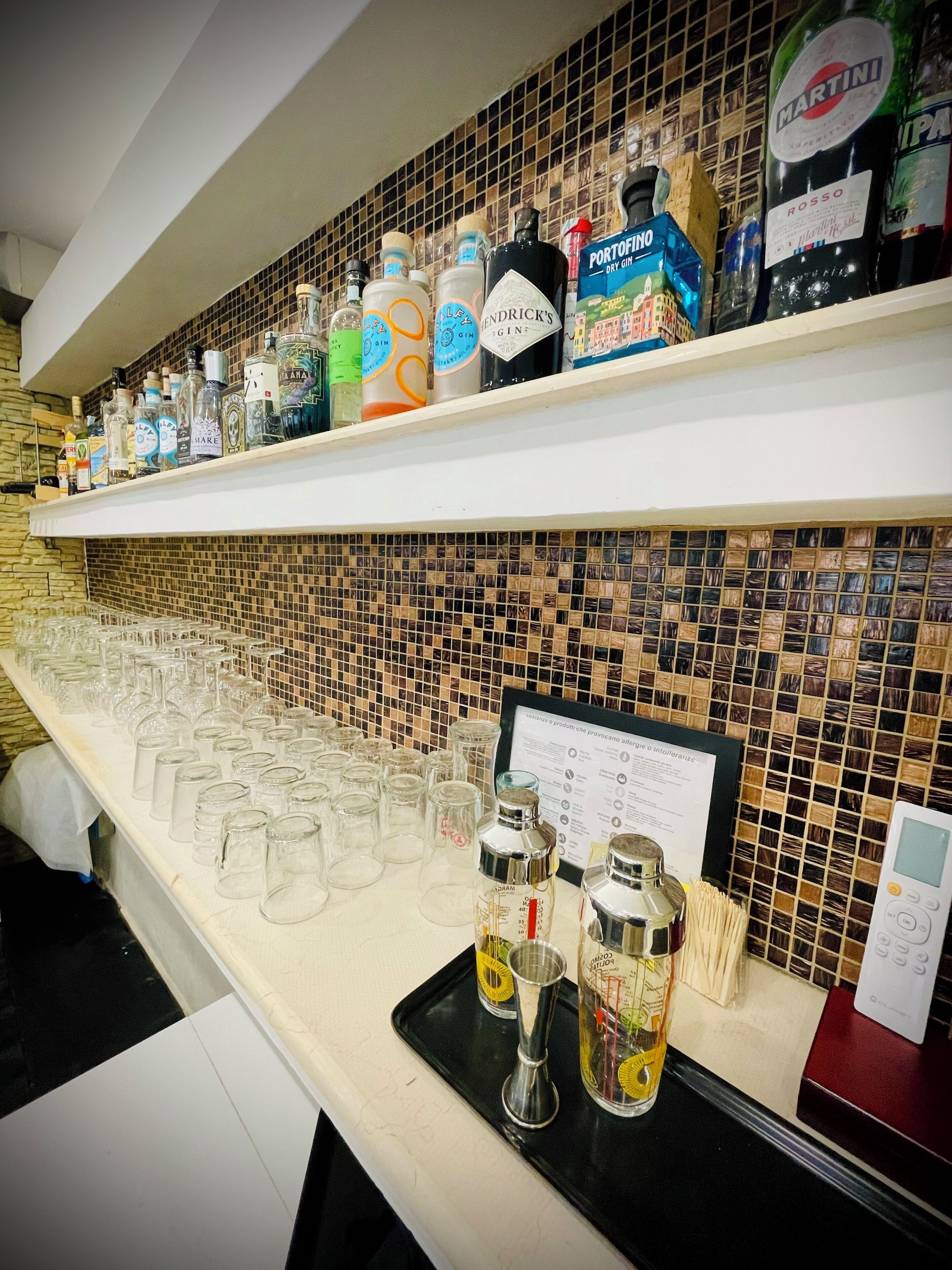 Zona de bar con estantes llenos de botellas de licores y una bandeja con vasos y copas para chupitos.