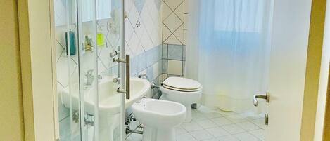 A modern bathroom with a glass shower enclosure, a toilet, a bidet, and a sink.