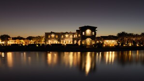 A large, illuminated mansion with a symmetrical facade, a central arched entrance, and a reflection in the calm water in front. - La Maison Bleue (El Gouna)